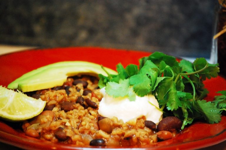 A rice bowl topped with seasoned black beans, diced avocado, fresh salsa, sour cream, and a lime wedge on a wooden table.