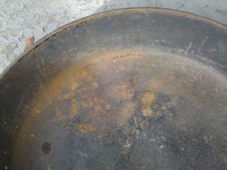 A well-seasoned cast-iron skillet with a glossy black surface resting on a stovetop next to a folded kitchen towel.