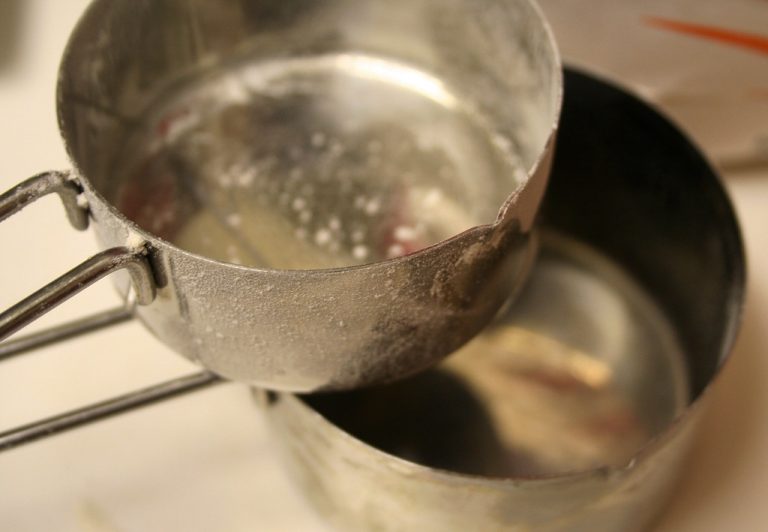 Flour being spooned into a dry measuring cup and leveled with a straight edge