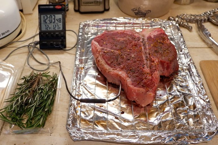 A pan-seared steak with a deep brown crust resting on a wooden cutting board next to a skillet of glossy pan sauce.