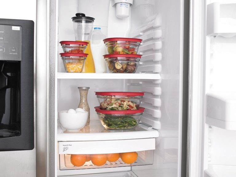 Cooked chicken and rice divided into shallow glass storage containers on a kitchen counter