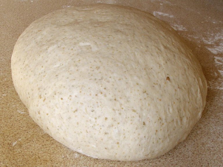 Bread dough rising in a glass bowl with visible air bubbles and a finger pressing a poke test into the surface