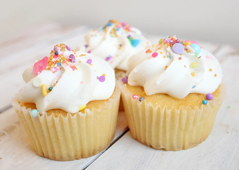 Vanilla cupcakes topped with white frosting and colorful sprinkles.